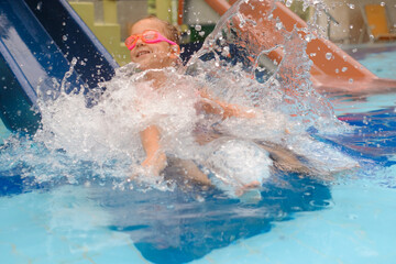 Wall Mural - Child sliding into the water in aqua park. Kid having fun and entertaining in indoor swimming pool. Toddler girl making splashes