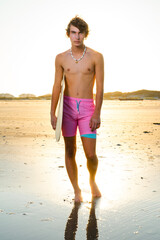 Handsome teenage beach model standing shirtless with surfboard during a golden sunset