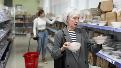 Wall Mural - Interested senior lady making purchases in local Asian store, choosing traditional ceramic ramen bowls on shelves with authentic dishware. High quality 4k footage