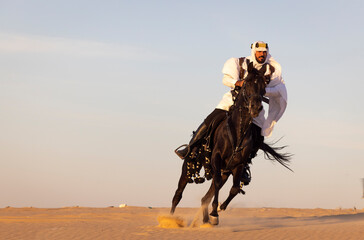 Wall Mural - Saudi man in a desert with his black stallion