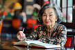 Thoughtful Elderly Asian Woman Writing in Notebook at a Cozy Cafe