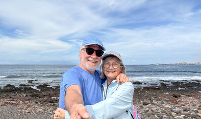 Wall Mural - Portrait of happy active senior caucasian couple together in outdoors at the sea beach enjoying vacation and retirement