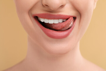 Canvas Print - Young woman licking her teeth on beige background, closeup