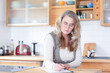 © Westend61 - Serious mature woman writing on paper in kitchen at home