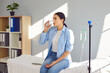 © Studio Romantic - Young woman with sterile needle in arm sitting on medical bed by pole with IV drip bottle, drinking glass of water and receiving vitamin therapy infusion to boost immune system and suppress infection