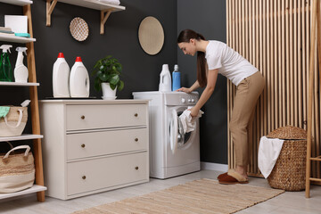 Wall Mural - Beautiful woman putting shirt into washing machine in laundry room