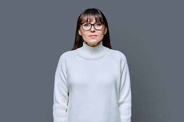 Wall Mural - Middle-aged beautiful serious woman in white sweater on gray studio background