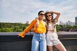 Fototapeta Londyn - appealing cheerful women in vibrant clothes with stylish sunglasses smiling at camera while on roof