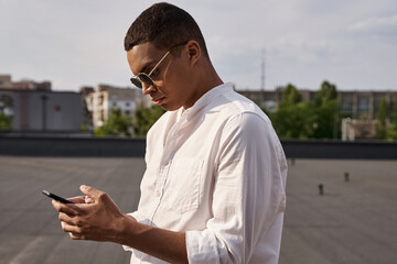 good looking young african american man in casual attire with sunglasses looking at smartphone