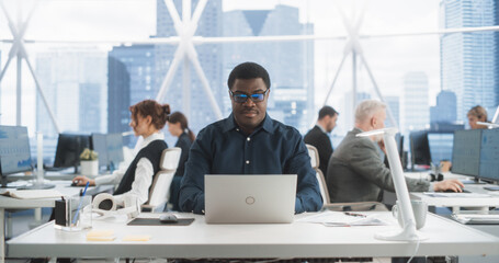 Poster - Succesful Black Man Typing On Laptop Computer In Bright Scyscraper Office With Diverse Employees In Downtown. Cheerful Male Programmer Coding In Modern Fintech Startup Workspace, Engineering Software