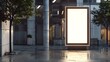 © Almultazam - Blank illuminating white billboard standing in a public street near modern building. copy space. vertical. mockup.