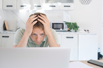 Wall Mural - Disappointed exhausted man freelancer working at home on laptop, overworked, needs rest and break. Dumbfounded male freelancer hold his head with hands, have problems while working on computer