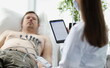 © H_Ko - Doctor taking cardiogram to patient on couch in clinic closeup. Holter monitoring concept