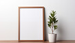 empty poster frame mockup on white wall with wooden mesh and small green plant.