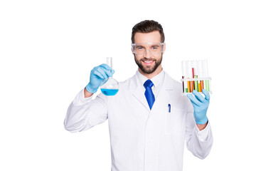 Portrait of cheerful handsome scientist with bristle in white lab coat, tie, protective glasses having test tubes and flask with multi-colored liquid, looking at camera over grey background