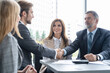 © opolja - Handshake in agreement against young business people in board room meeting.