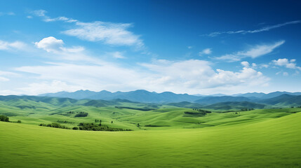 Wall Mural - Paysage d'une prairie avec de l'herbe verte, des montagnes en arrière-plan et un beau ciel bleu avec nuages. Fond d'écran, décor, paysage calme. Pour conception et création graphique.