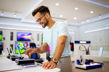 Happy young man trying out new smart phone, digital devices. Tech store interior.