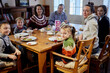 © Pavel Losevsky - Three adults and four children sit at wooden table in room