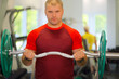 Young strong man holds barbell in modern gym with fitness equipment