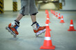 Legs of roller skater posing on floor near orange cones in indoor parking