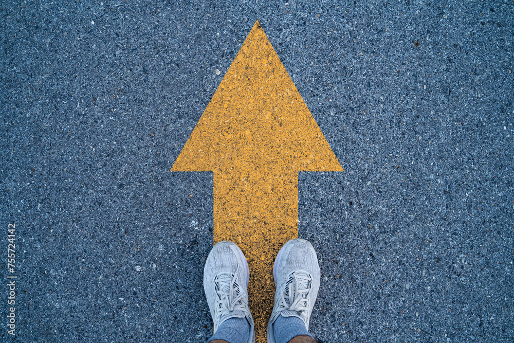 Runner standing on asphalt road with yellow arrow for go ahead and ...