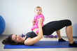 Happy woman lying on her back with baby on her stomach doing exercises in the gym
