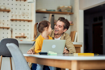 Happy family of two, a girl sitting on her dad's lap while he's taking a break from work