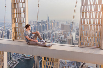 Roofer sits on concrete cross beam of Cayan Tower (Infinity Tower) in Dubai, UAE