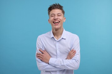 Poster - Young man with crossed arms laughing on light blue background