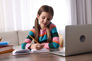 Wall Mural - E-learning. Cute girl taking notes during online lesson at table indoors