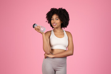 Wall Mural - Smiling black woman with water bottle, sportswear, pink background