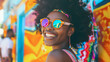 A woman with a colorful headband and sunglasses is smiling. She is wearing a striped tank top and has her hair in a bun