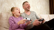 © Vladislav - A father spends time with his little daughter, sitting on the sofa and playing a game console. Weekend activities, free time, home entertainment and video games concept.