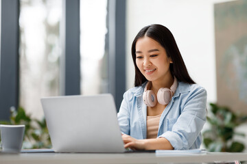 Poster - Smiling asian freelancer woman with headphones working on laptop