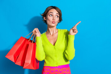 Sticker - Photo of young funny girl shopaholic pointing finger empty space plump lips red packages shopping mall isolated on blue color background