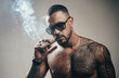 © Volodymyr - Portrait of handsome man smoking cigar. Tattooed man with cigar. Portrait of a mafia boss with a strong bare torso smoking a cigar. Mafia boss.