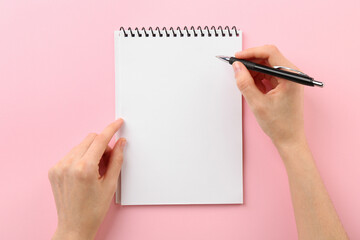 Canvas Print - Woman writing in notebook on pink background, top view