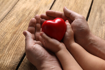 Sticker - Father and his child holding red decorative heart at wooden table, closeup