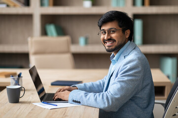 Aufkleber - Indian businessman using laptop sits at desk smiling to camera