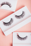 Fototapeta Tulipany - Different fake eyelashes in boxes on trendy pastel pink background. Makeup accessories and beauty cosmetics products for women. Top view, flat lay.