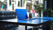 A vibrant cobalt blue laptop adds a pop of color to a minimalist table, inspiring creativity and innovation in a bustling urban environment.