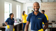© Studio Nova - Smiling man in a cleaning service uniform with colleagues in the background, indicating a professional cleaning team at work.