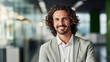 © MP Studio - Smiling man with curly hair, wearing a green shirt, arms crossed, standing in a modern office setting.