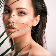 Wall Mural - young beautiful woman with green leaves near face. white model with clean, health skin of face.