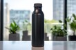 Matte black water bottle stands on a white table, harmonizing with the modern office ambiance, highlighted by natural light and indoor plants