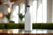 Matte white water bottle stands on a wooden table, offering a touch of simplicity and elegance against the lively backdrop of a sunlit cafe interior