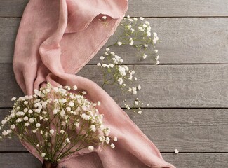 Canvas Print - Hello spring concept. Top view photo of pink soft plaid and gypsophila flowers on grey wooden table background with copyspace, Generative AI