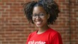 Volunteer woman smiling in red shirt - An enthusiastic young woman with glasses and curly hair wears a 'volunteer' shirt, exuding a friendly and dedicated persona