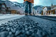 Close up of an asphalt road construction worker working on a new asphalt street in a residential area, with a mountain landscape background